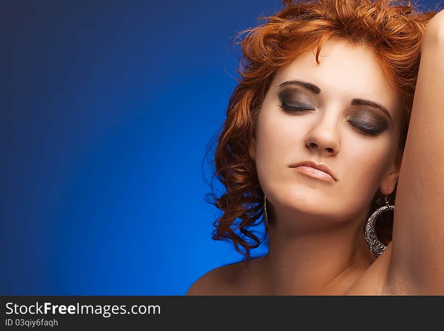 Portrait of young beautiful long-haired closed-eyed redhead woman on blue background. Portrait of young beautiful long-haired closed-eyed redhead woman on blue background