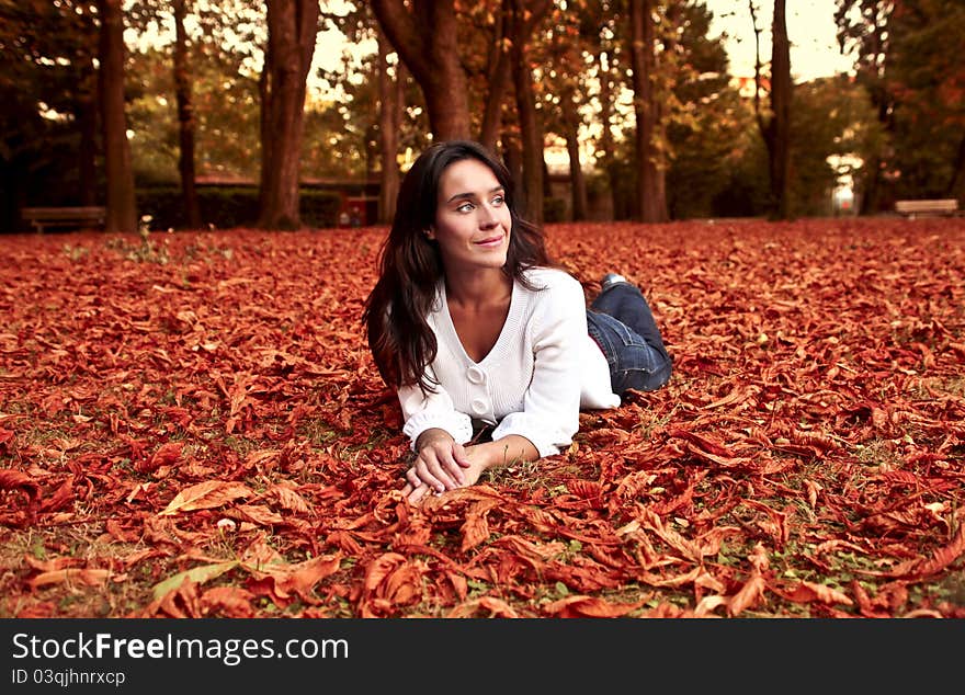 Beautiful smiling woman lying in a park in autumn. Beautiful smiling woman lying in a park in autumn