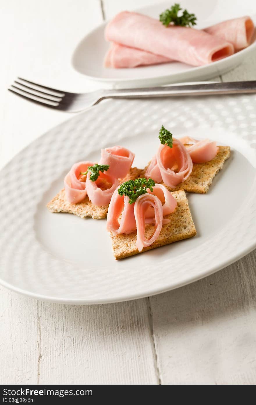 Photo of cracker appetizer with ham and parsley on white wooden table. Photo of cracker appetizer with ham and parsley on white wooden table