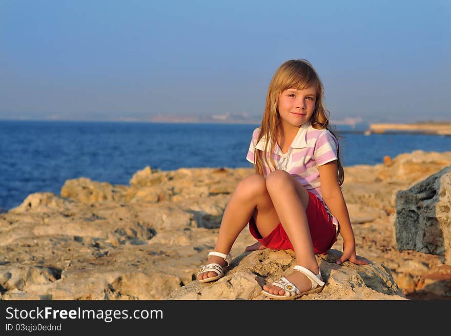 A girl sitting on rocks by the sea at sunset. A girl sitting on rocks by the sea at sunset