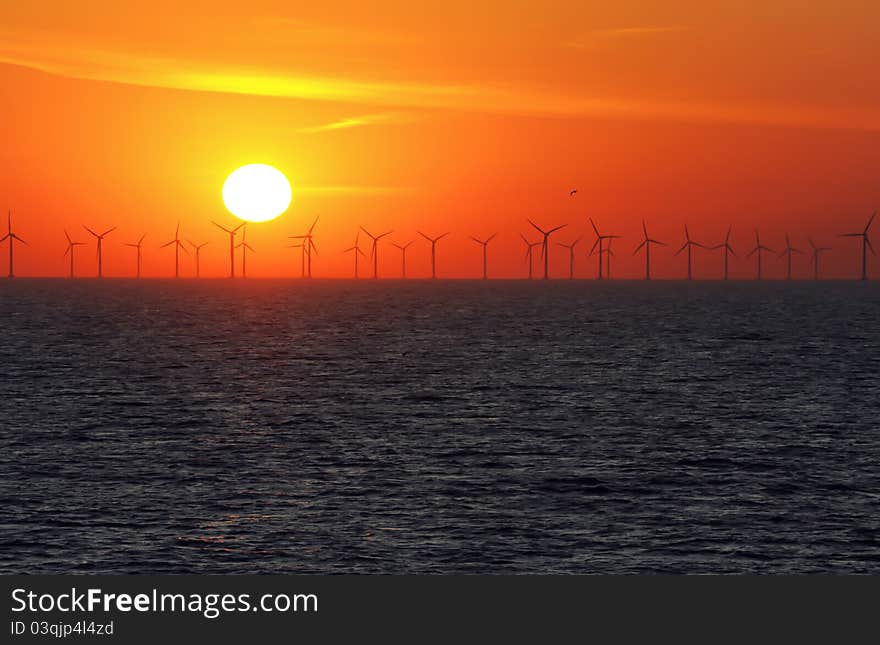 Silhouette of wind power stations over the sea at sunset