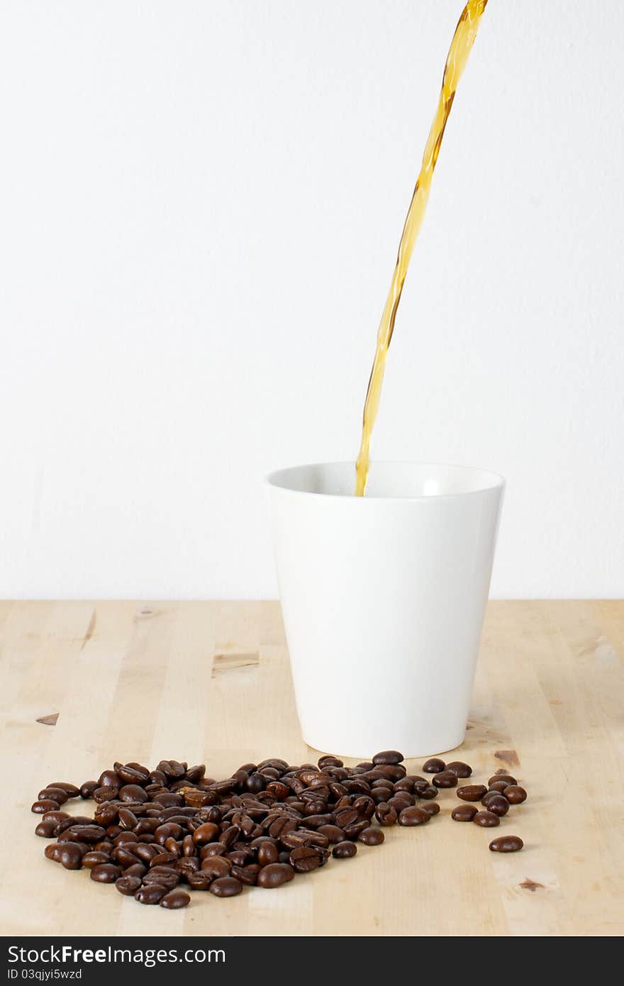 Picture of coffee beans and a white cup on a table. Coffee being poured in the cup. Picture of coffee beans and a white cup on a table. Coffee being poured in the cup