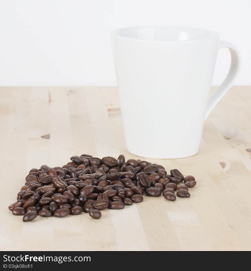 Picture of coffee beans and a white cup on a table. Picture of coffee beans and a white cup on a table