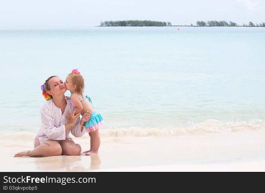 A Baby Girl Is Kissing Her Mother On The Beach