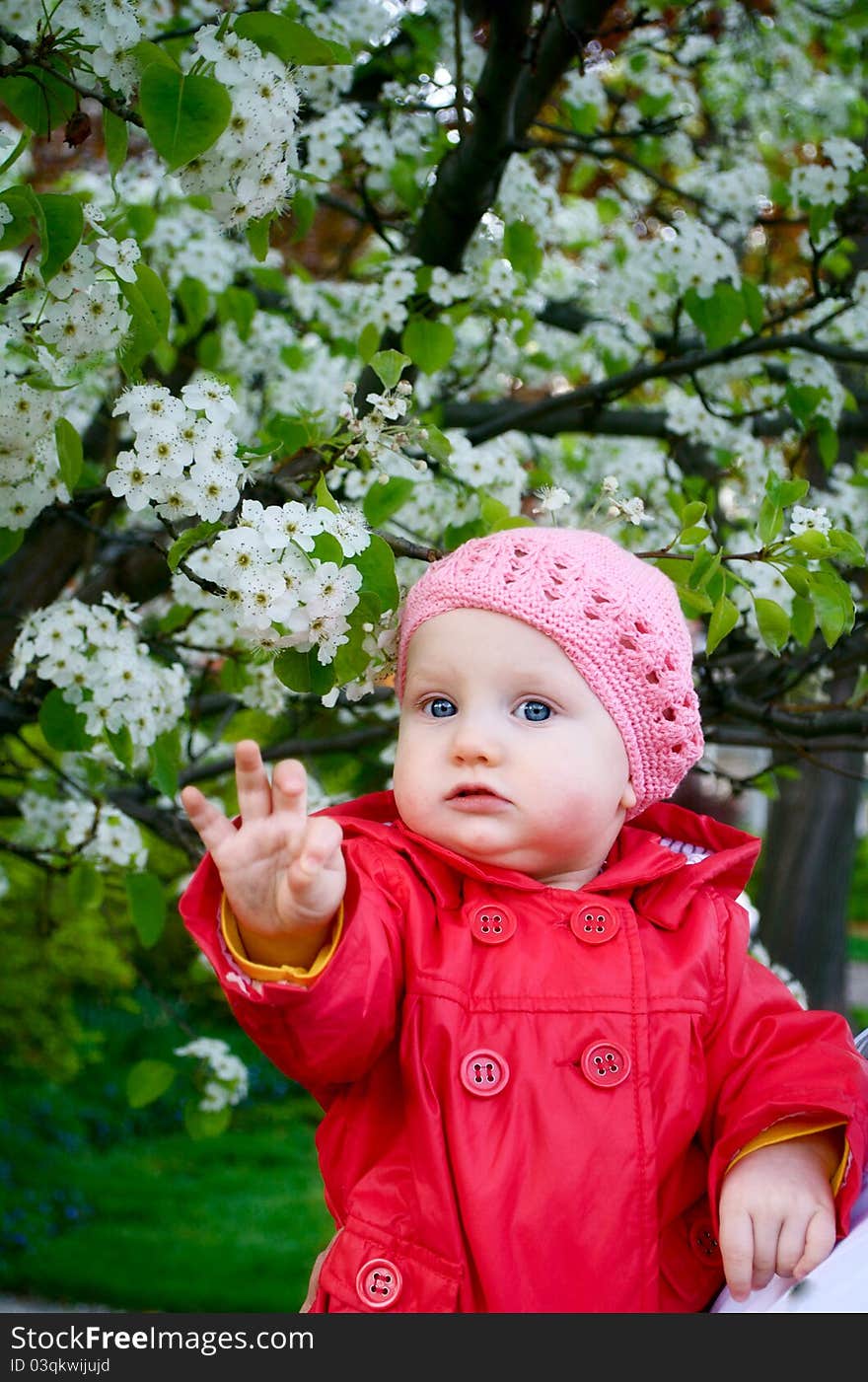 A baby girl in the garden next to blossom tree