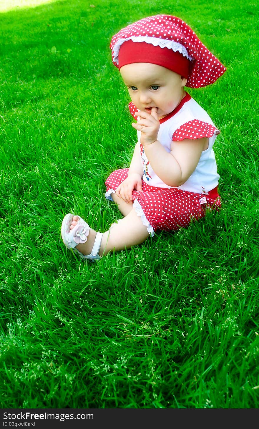 A cute baby girl is sitting on the grass on summer day. A cute baby girl is sitting on the grass on summer day