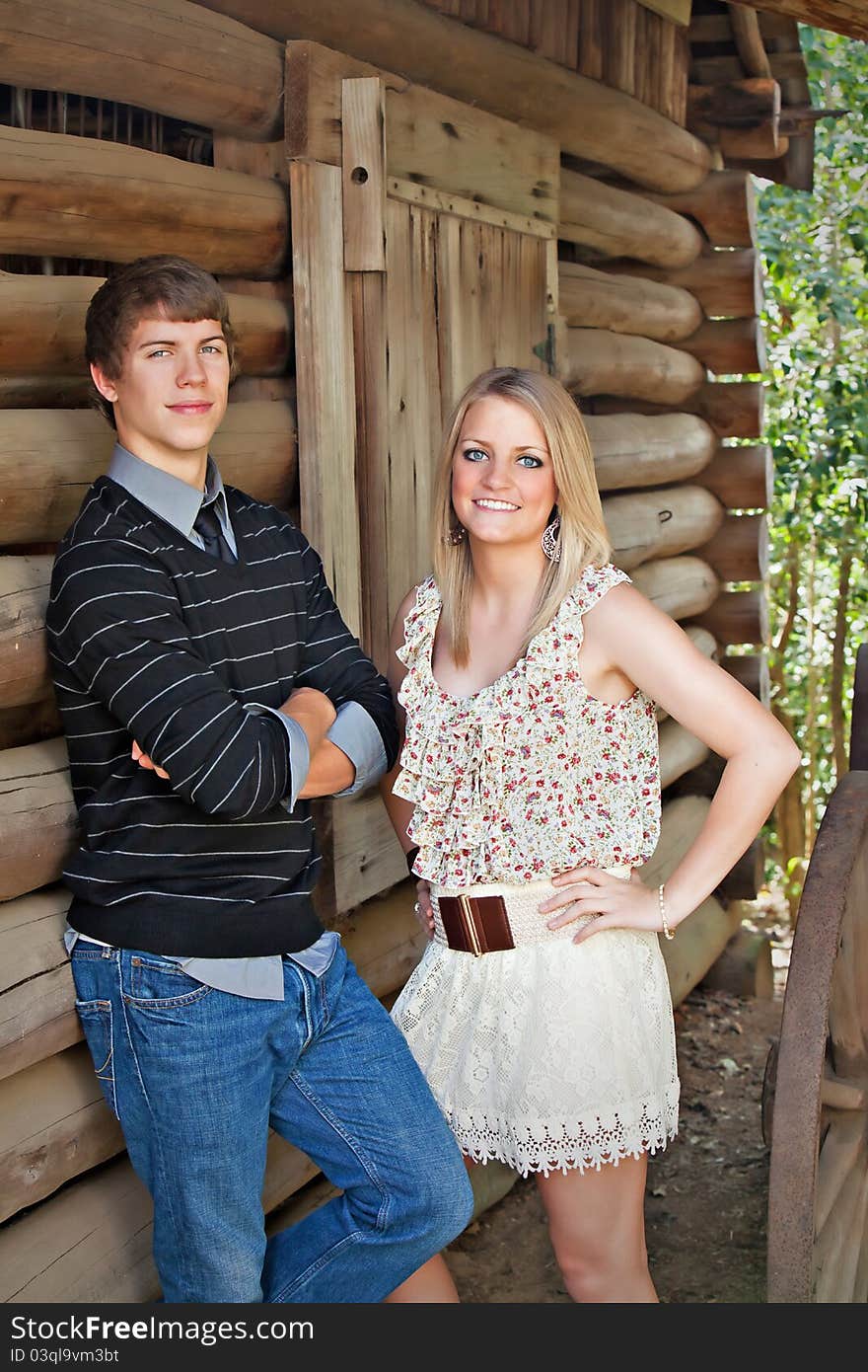 Beautiful teenage girl and teen boy standing next to log wall. Beautiful teenage girl and teen boy standing next to log wall.