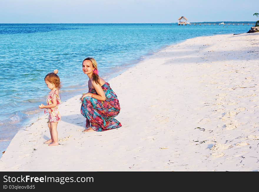 A young mother is playing with a baby girl on the beach of the ocean. A young mother is playing with a baby girl on the beach of the ocean