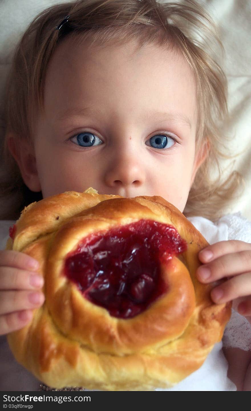 A cute little girl with big blue eyes is eating a big pie. A cute little girl with big blue eyes is eating a big pie