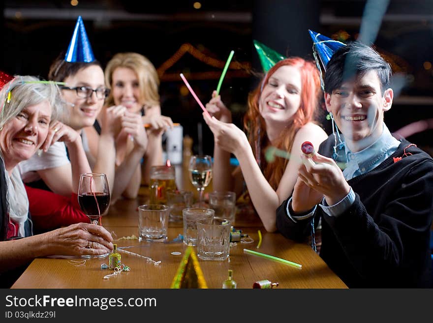 A group of men and women of mixed ages, wearing party hats and popping streamers. All are looking to the camera, one male is firing the streamers towards camera. A group of men and women of mixed ages, wearing party hats and popping streamers. All are looking to the camera, one male is firing the streamers towards camera