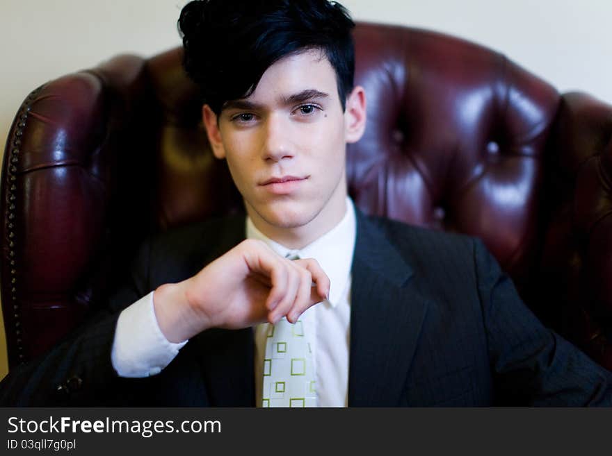 A young handsome male dressed in a suit, seated on a plush leather chair, looking directly to camera. A young handsome male dressed in a suit, seated on a plush leather chair, looking directly to camera.