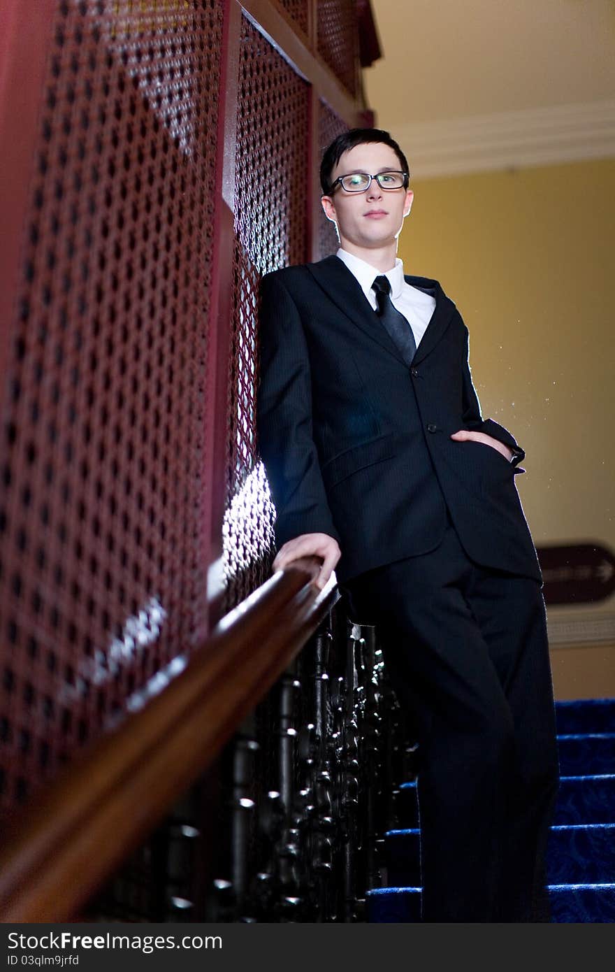 A young well dressed man leans against an elevator cage, left hand in pocket. A young well dressed man leans against an elevator cage, left hand in pocket.