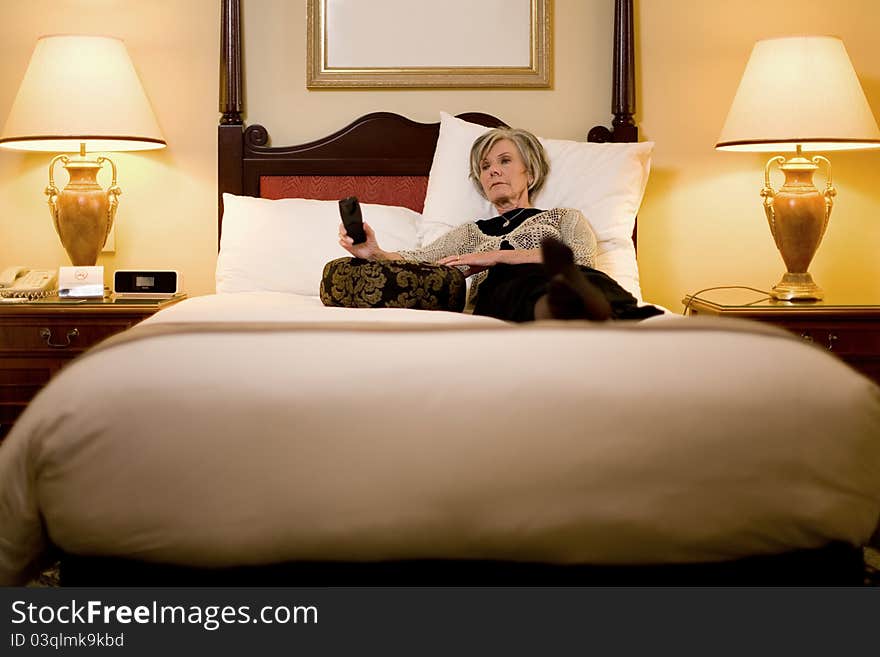 A mature female traveller relaxing on her hotel bed watching television