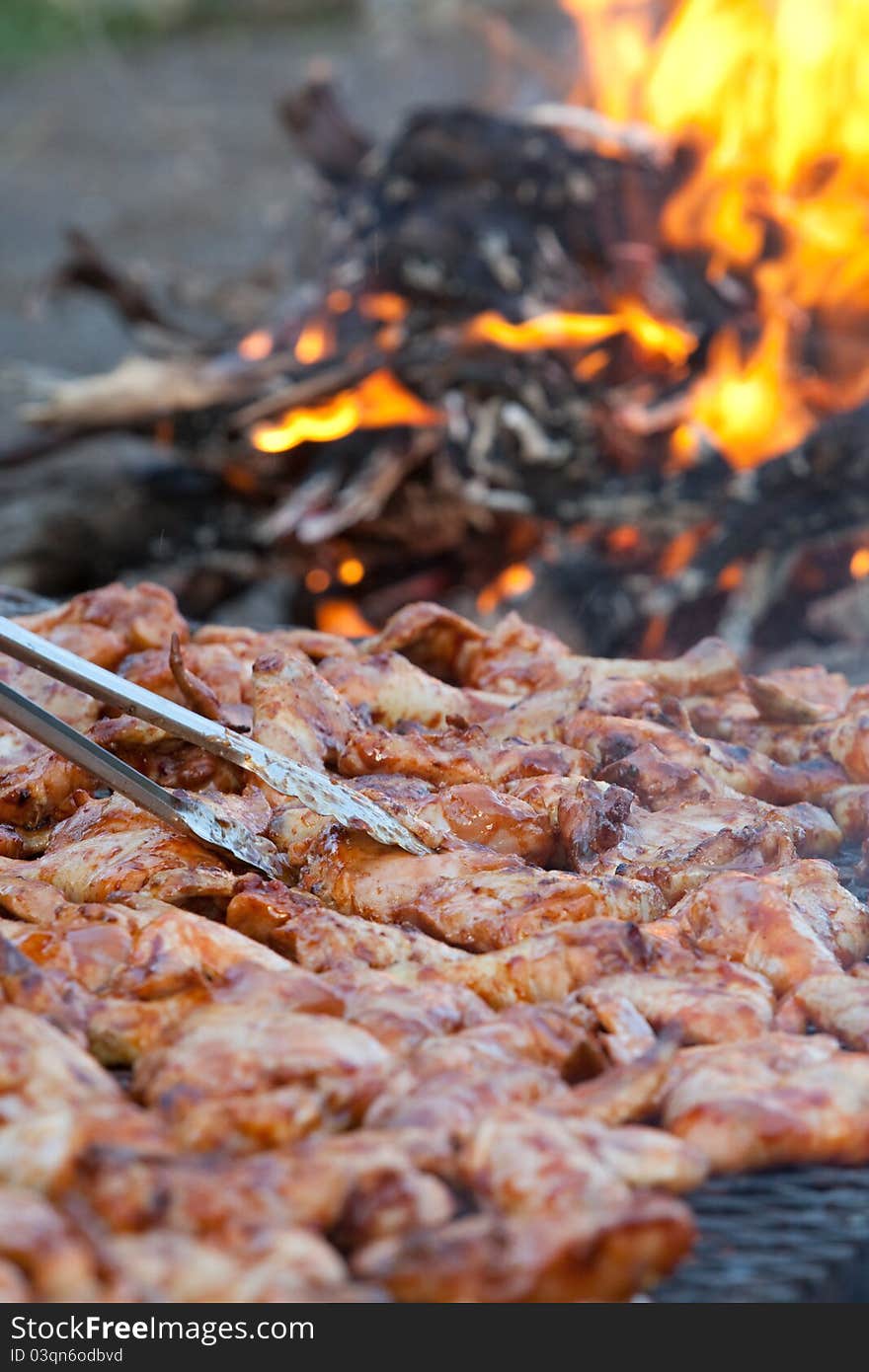 A vertical close up of chicken pieces being grilled on an open fire outdoors. A vertical close up of chicken pieces being grilled on an open fire outdoors