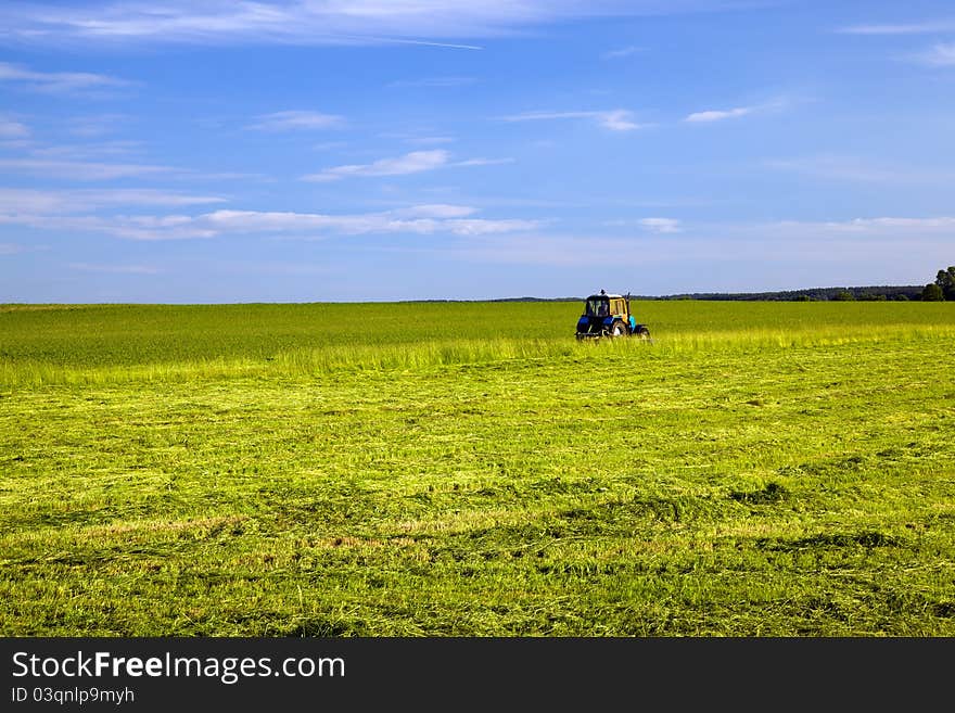 The tractor which is going across the field and mowing down an evolved green grass. The tractor which is going across the field and mowing down an evolved green grass