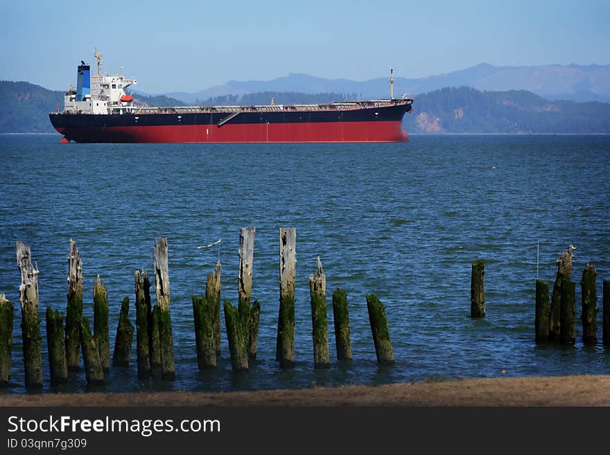 A red cargo ship anchored before continuing on up river with territorial hills in the background and old pilings in the foreground. A red cargo ship anchored before continuing on up river with territorial hills in the background and old pilings in the foreground.