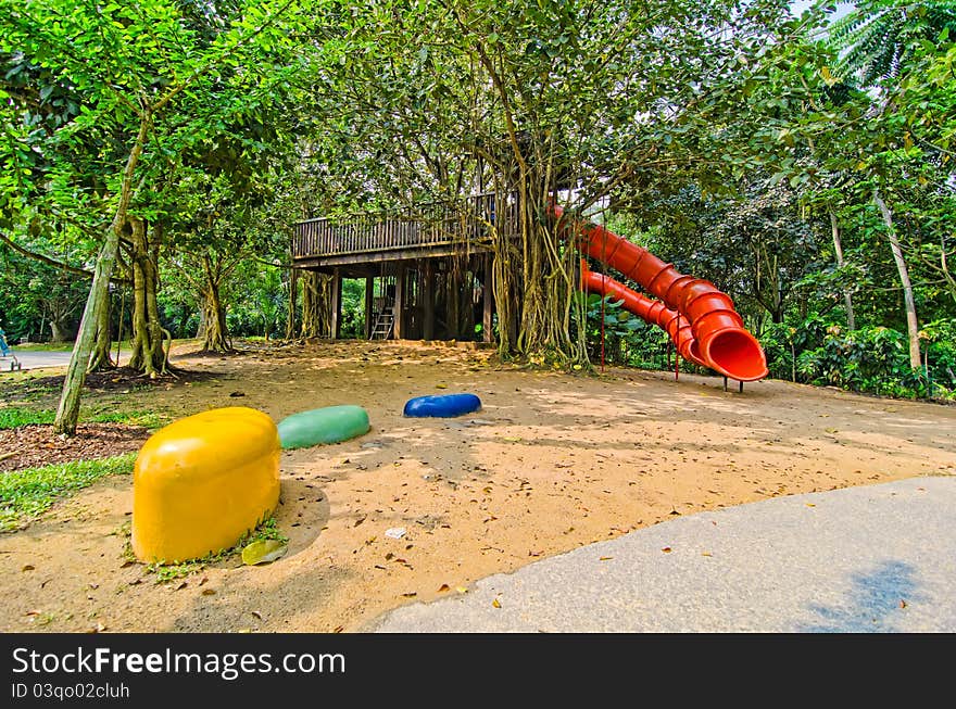Photo of red colorful slide and a treehouse in garden or backyard of nursery school play area with colorful rocks. Photo of red colorful slide and a treehouse in garden or backyard of nursery school play area with colorful rocks