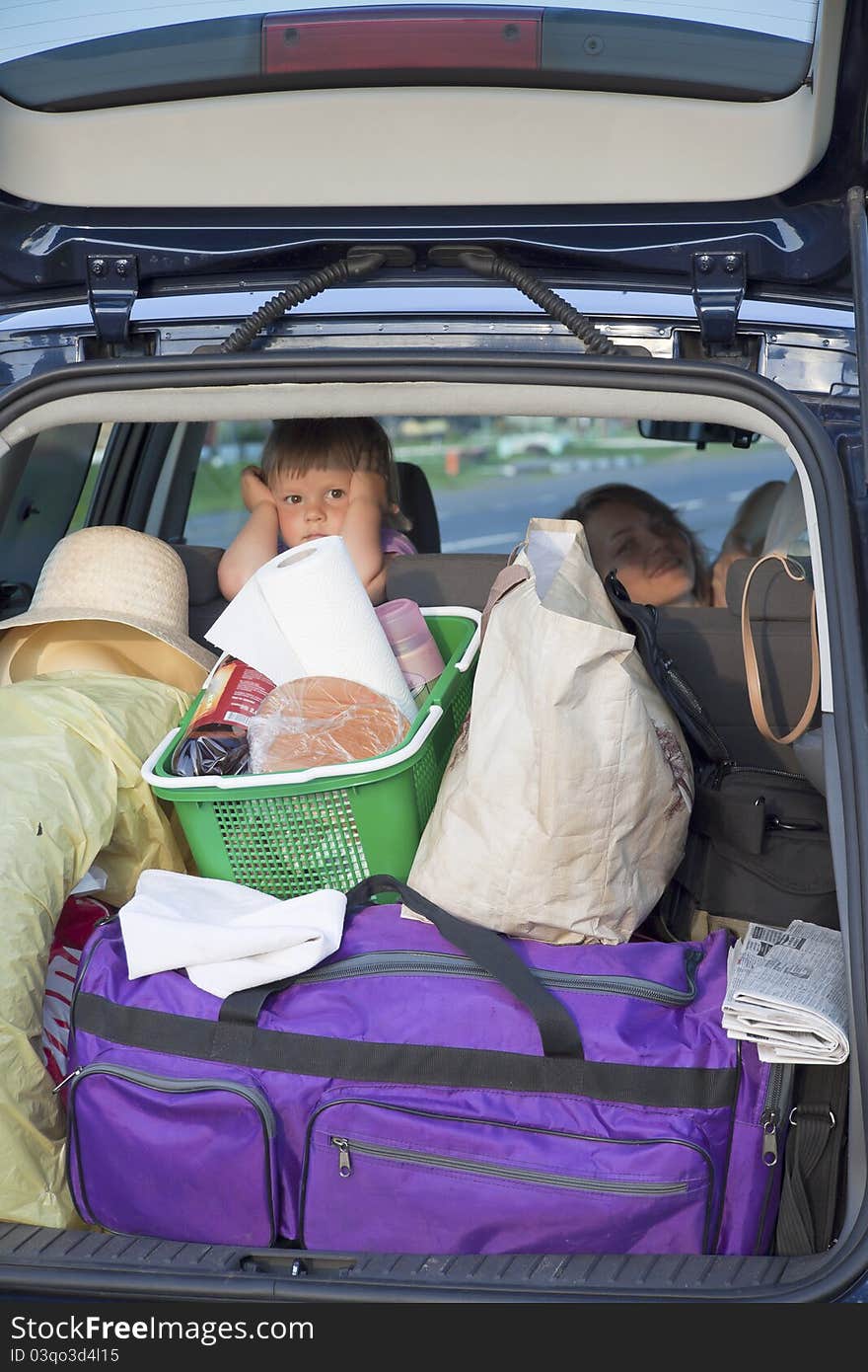 The tired child looks out of a car luggage carrier where the luggage lays. The tired child looks out of a car luggage carrier where the luggage lays