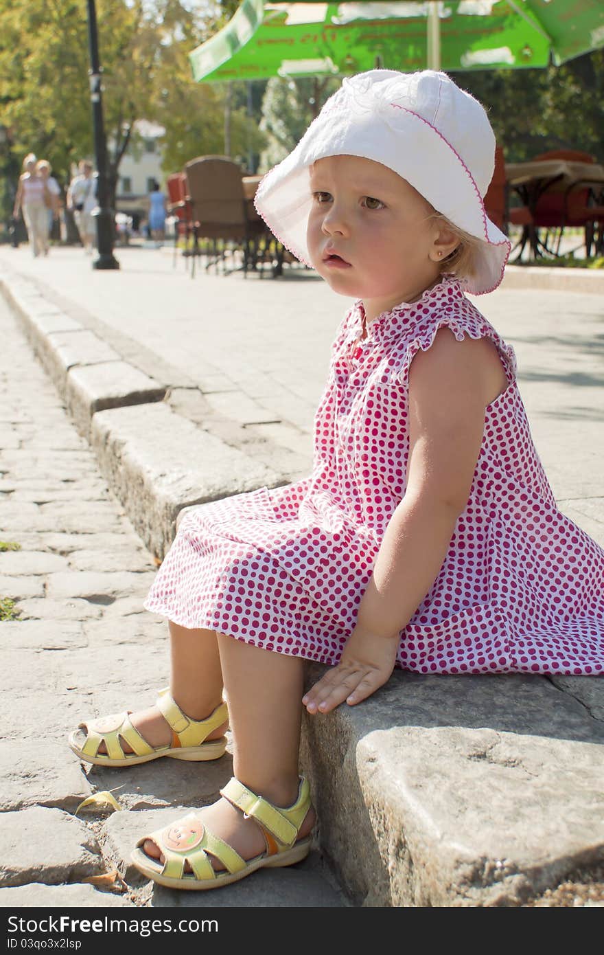 The little girl sits on the brink of a roadway. The little girl sits on the brink of a roadway