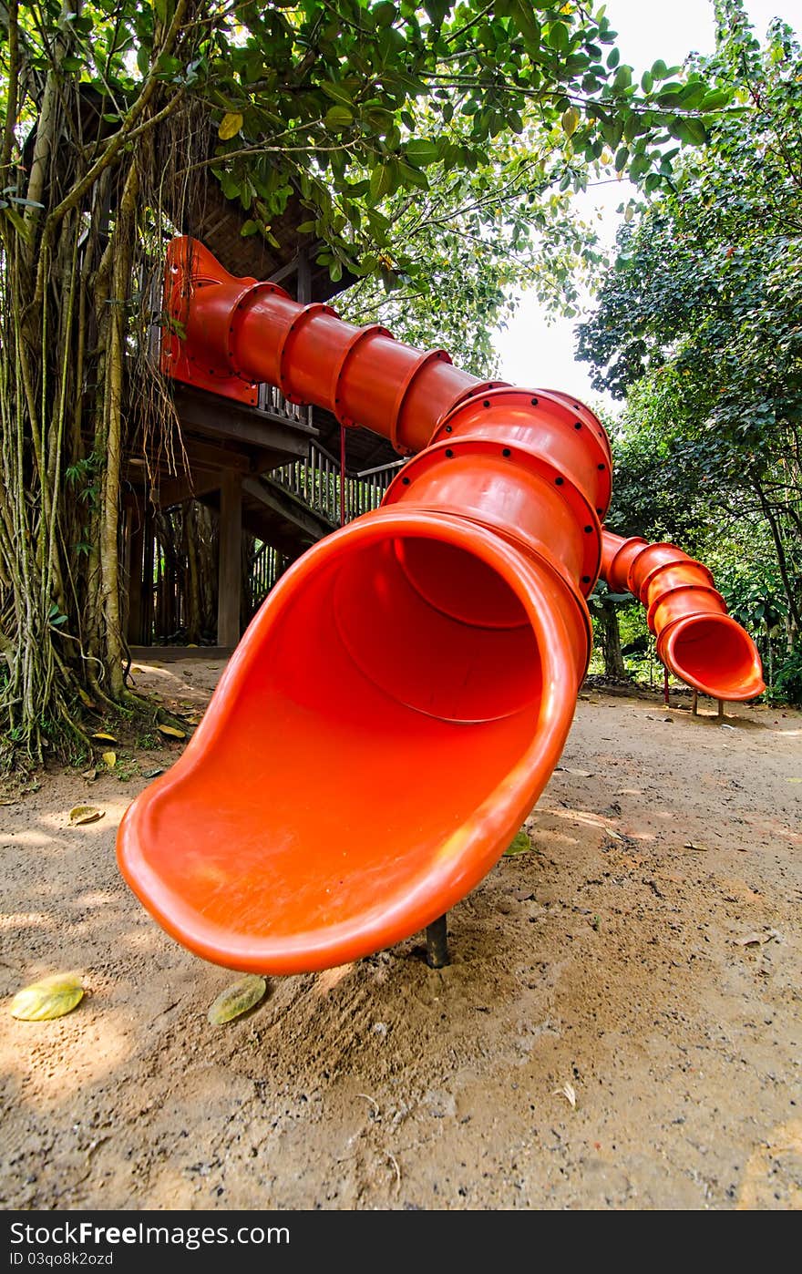 Photo of red colorful slide and a treehouse in garden or backyard of nursery school play area. Photo of red colorful slide and a treehouse in garden or backyard of nursery school play area