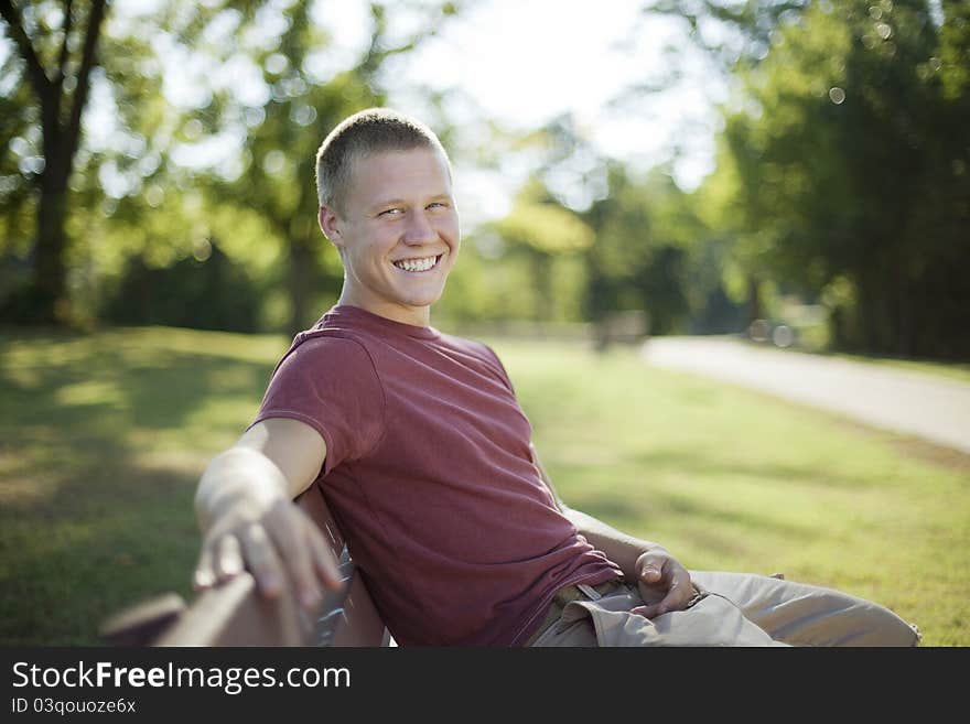 Handsome young man sitting on a bench smiling. Candid. Handsome young man sitting on a bench smiling. Candid.