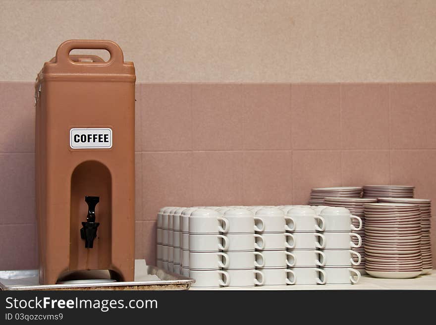 Plastic coffee dispenser sitting on a dirty drip pan. White coffee mugs and snack plates are also shown.