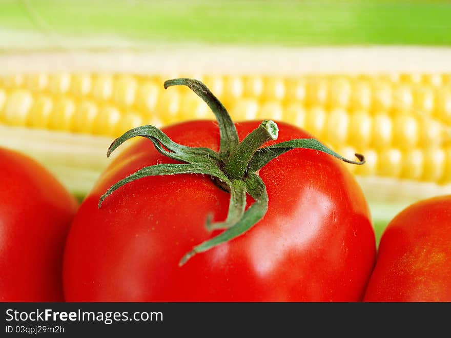 Macro of red tomato with green leaves and corn on blurred background. Macro of red tomato with green leaves and corn on blurred background