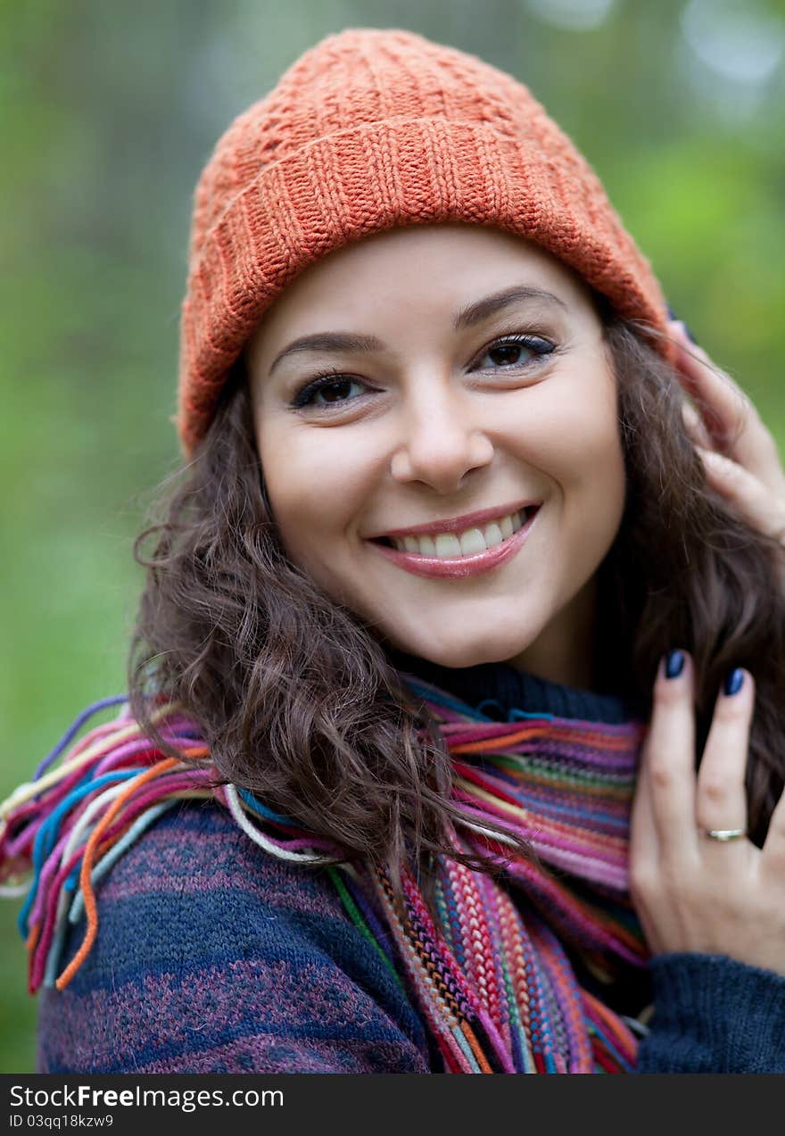 A girl in an orange hat and a bright scarf posing against a background of trees. A girl in an orange hat and a bright scarf posing against a background of trees