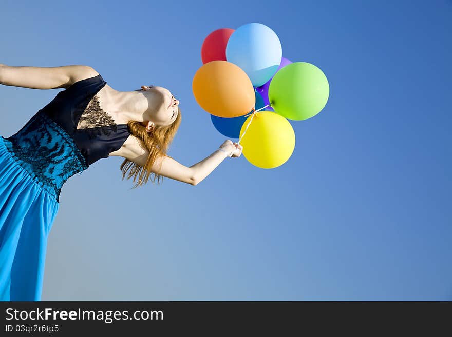 Redhead girl with colour balloons at blue sky background.