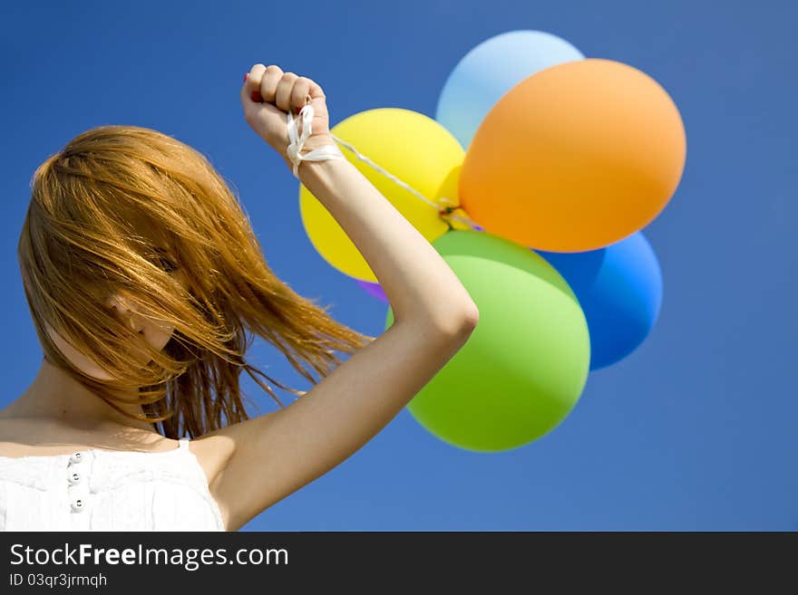 Redhead girl with colour balloons at blue sky background.