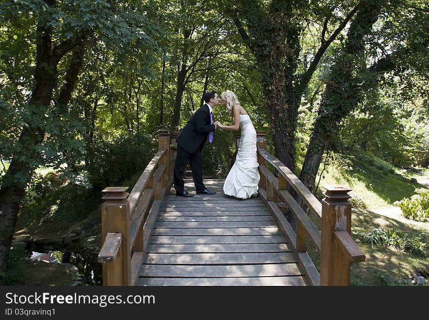 Boy and girl kissing on a wooden bridge in Green Forest. Boy and girl kissing on a wooden bridge in Green Forest