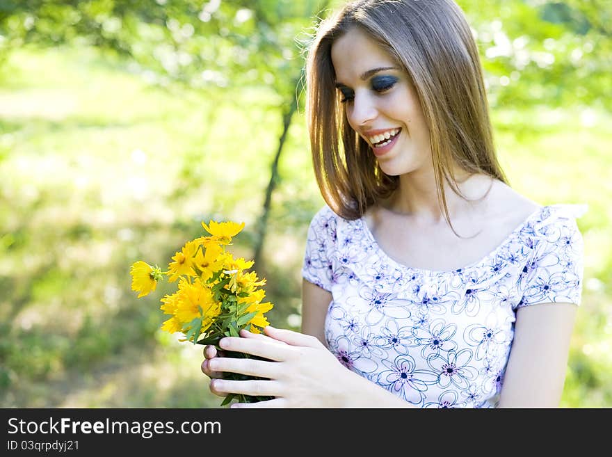 Portrait of a happy young girl smiling and holding orange flowers in her hands outdoor in summertime