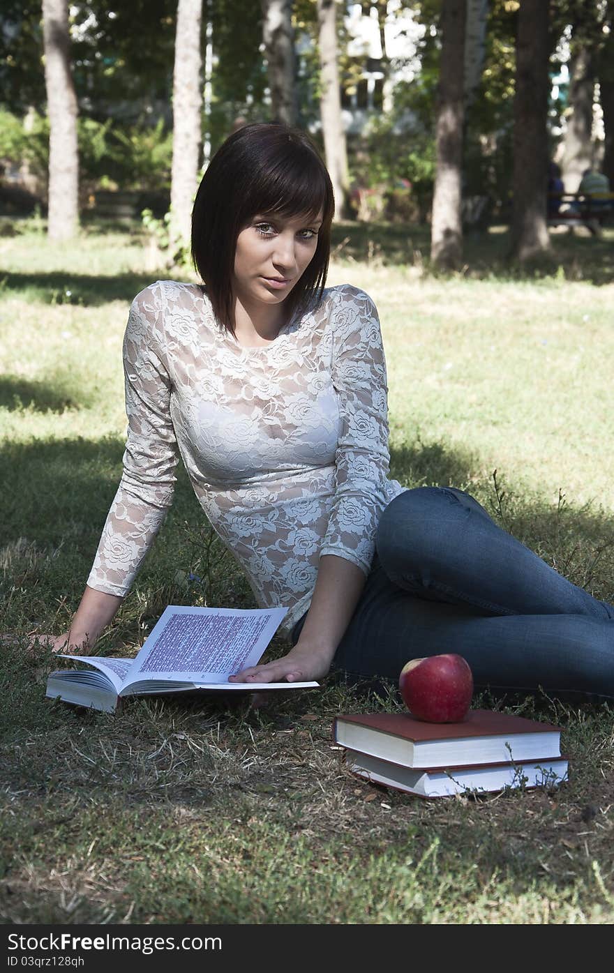 Young woman sitting on the grass and holding a book photographed in park. Young woman sitting on the grass and holding a book photographed in park