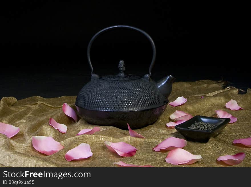 Black Chinese teapot with green tea and rose petals scattered.