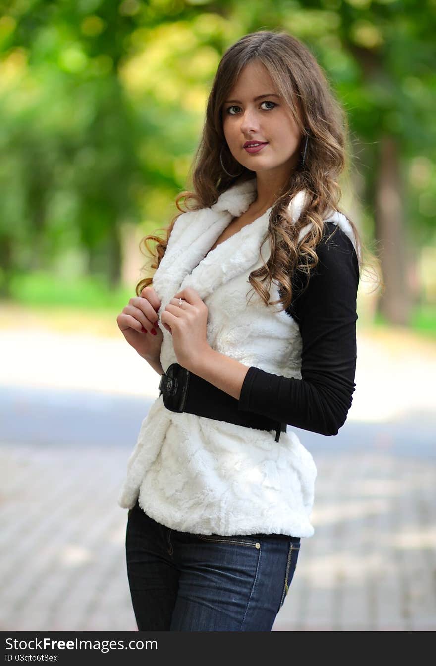 Portrait of the beautiful young girl with long hair, in the park, a holding hand with manicure on a white fur coat against green trees. Portrait of the beautiful young girl with long hair, in the park, a holding hand with manicure on a white fur coat against green trees