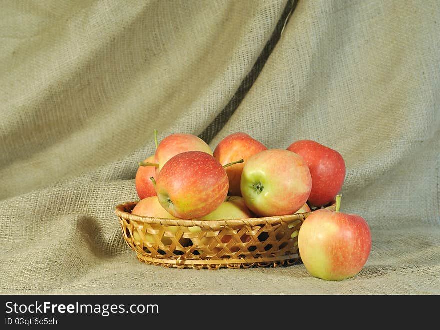 The autumn topic. In the foreground are red apples. They lie in the basket wich is on the table. The table is covered by rough stuff. This stuff creates background. The autumn topic. In the foreground are red apples. They lie in the basket wich is on the table. The table is covered by rough stuff. This stuff creates background.