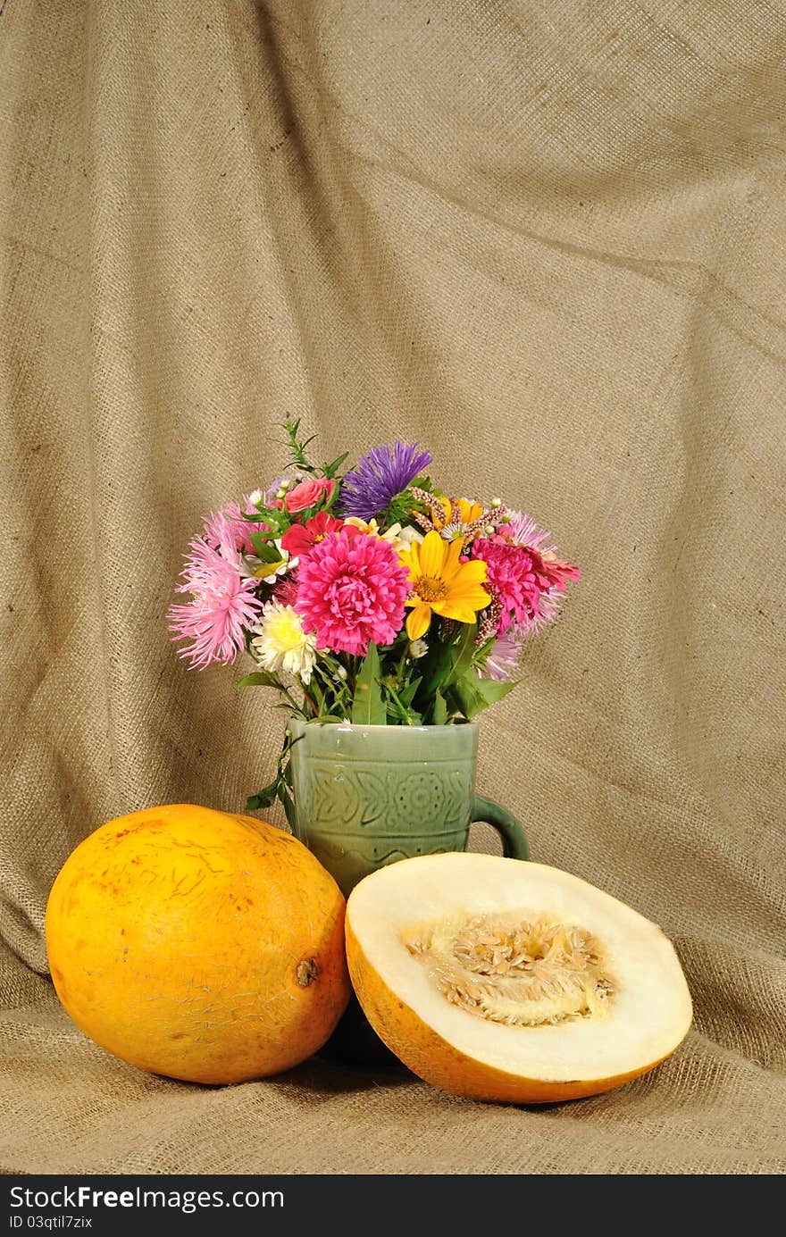 The autumn topic. In the foreground is bouquet of wild and cultivated flowers and orange melon. They are on the table covered by rough stuff. This staff creates background. The autumn topic. In the foreground is bouquet of wild and cultivated flowers and orange melon. They are on the table covered by rough stuff. This staff creates background.