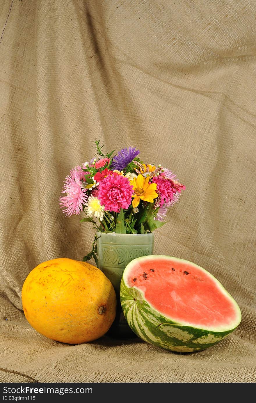 The autumn topic. In the foreground is bouquet of wild and cultivated flowers and melon. They are on the table covered by rough stuff. This staff creates background. The autumn topic. In the foreground is bouquet of wild and cultivated flowers and melon. They are on the table covered by rough stuff. This staff creates background.