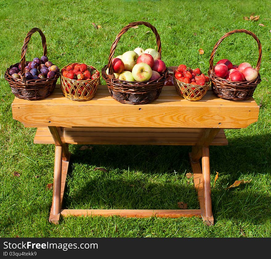 Baskets with plums, strawberryes and apples on the table outdoor. Baskets with plums, strawberryes and apples on the table outdoor