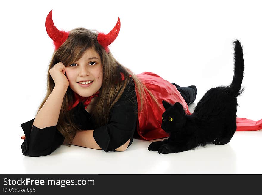 A happy tween girl dressed as a devil happily laying beside a black Halloween cat. A happy tween girl dressed as a devil happily laying beside a black Halloween cat.