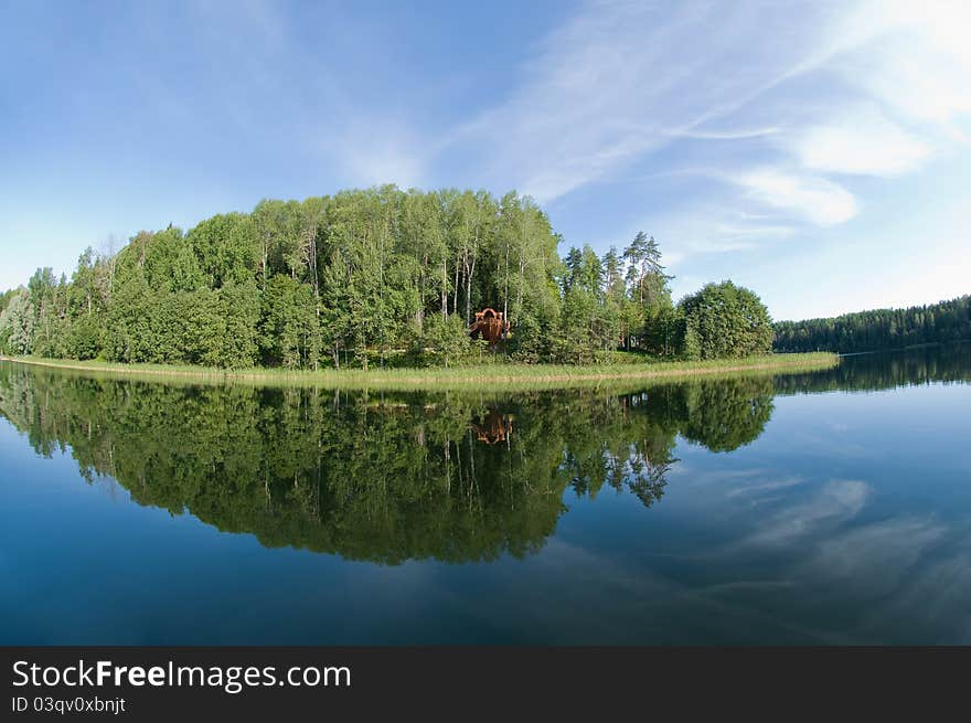 Unspoilt forested hills reflecting in a calm blue lake, with blue skies and white fluffy clouds above. Unspoilt forested hills reflecting in a calm blue lake, with blue skies and white fluffy clouds above.