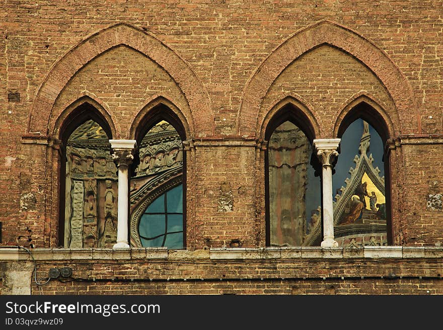 The large windows in a building across from the main cathedral in Siena, Italy, with interesting reflections of the cathedral in them. The large windows in a building across from the main cathedral in Siena, Italy, with interesting reflections of the cathedral in them.