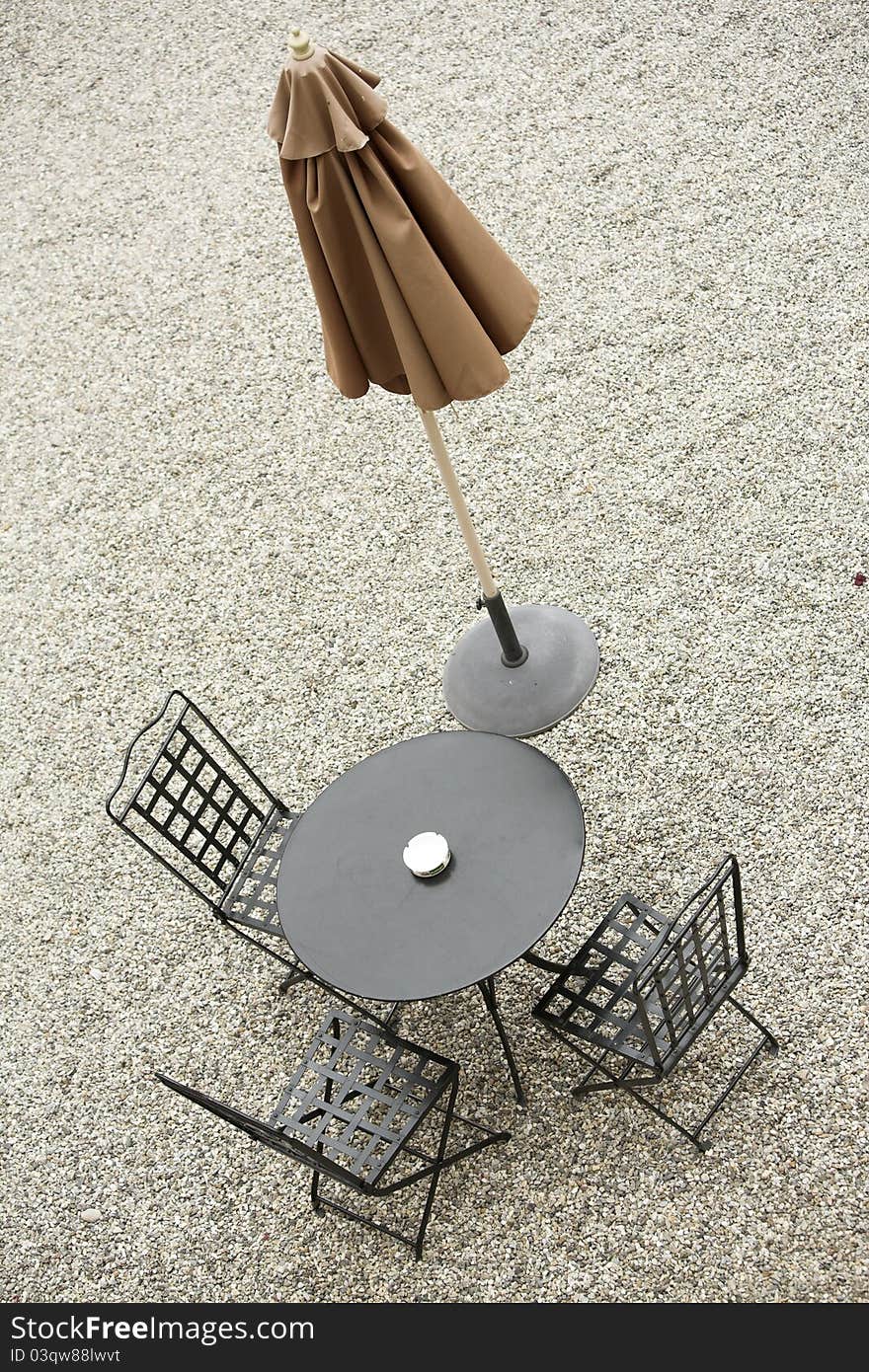 Iron outdoor table and chairs, with closed brown parasol. Iron outdoor table and chairs, with closed brown parasol