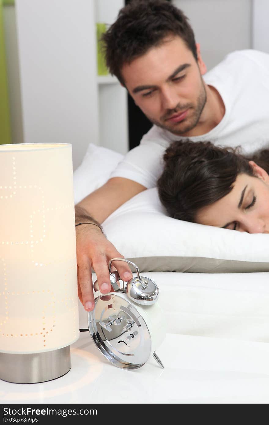 Couple in bed waking up, the men switches off the alarm clock