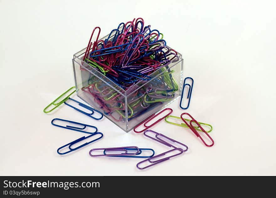 Brightly colored paperclips spilling out of a square, clear acrylic holder. Brightly colored paperclips spilling out of a square, clear acrylic holder.