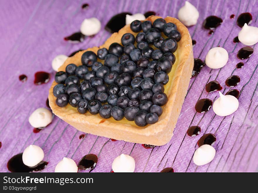 Heart-shaped tart with cream and blueberries served on a glass plate decorated with meringues and topping. Heart-shaped tart with cream and blueberries served on a glass plate decorated with meringues and topping