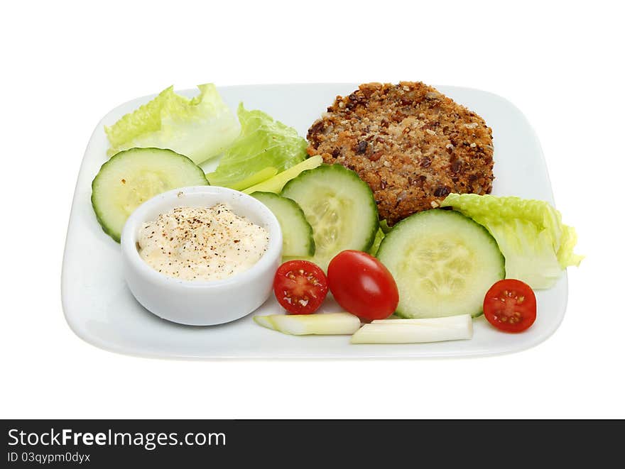 Fish cake and salad with a ramekin of mayonnaise on a plate isolated against white