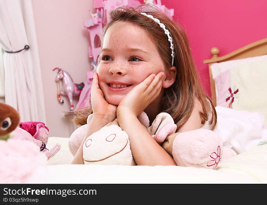 A happy young girl lies on a bed in a bright pink room.