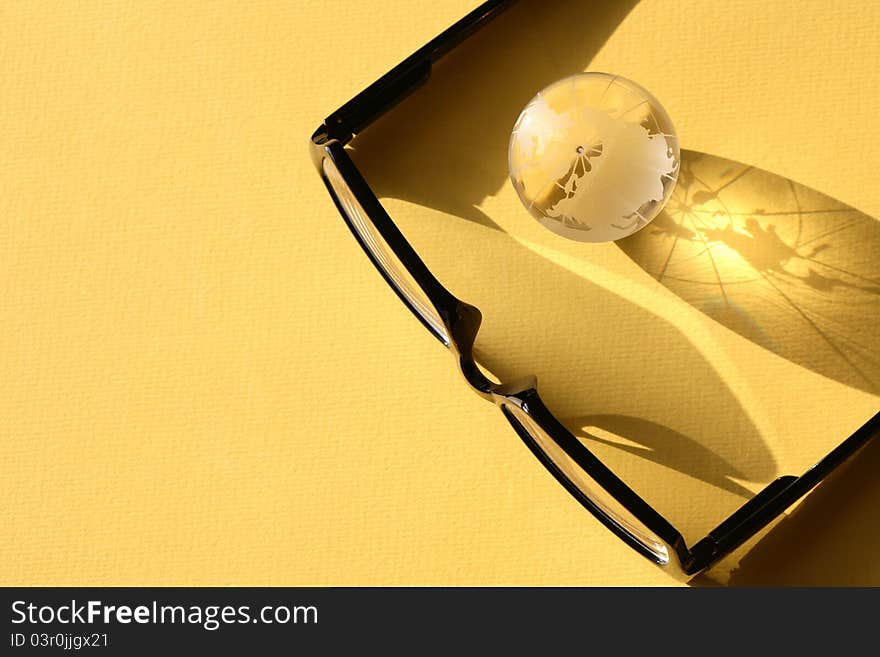 Business concept. Glass globe near modern black spectacles on yellow surface. Business concept. Glass globe near modern black spectacles on yellow surface