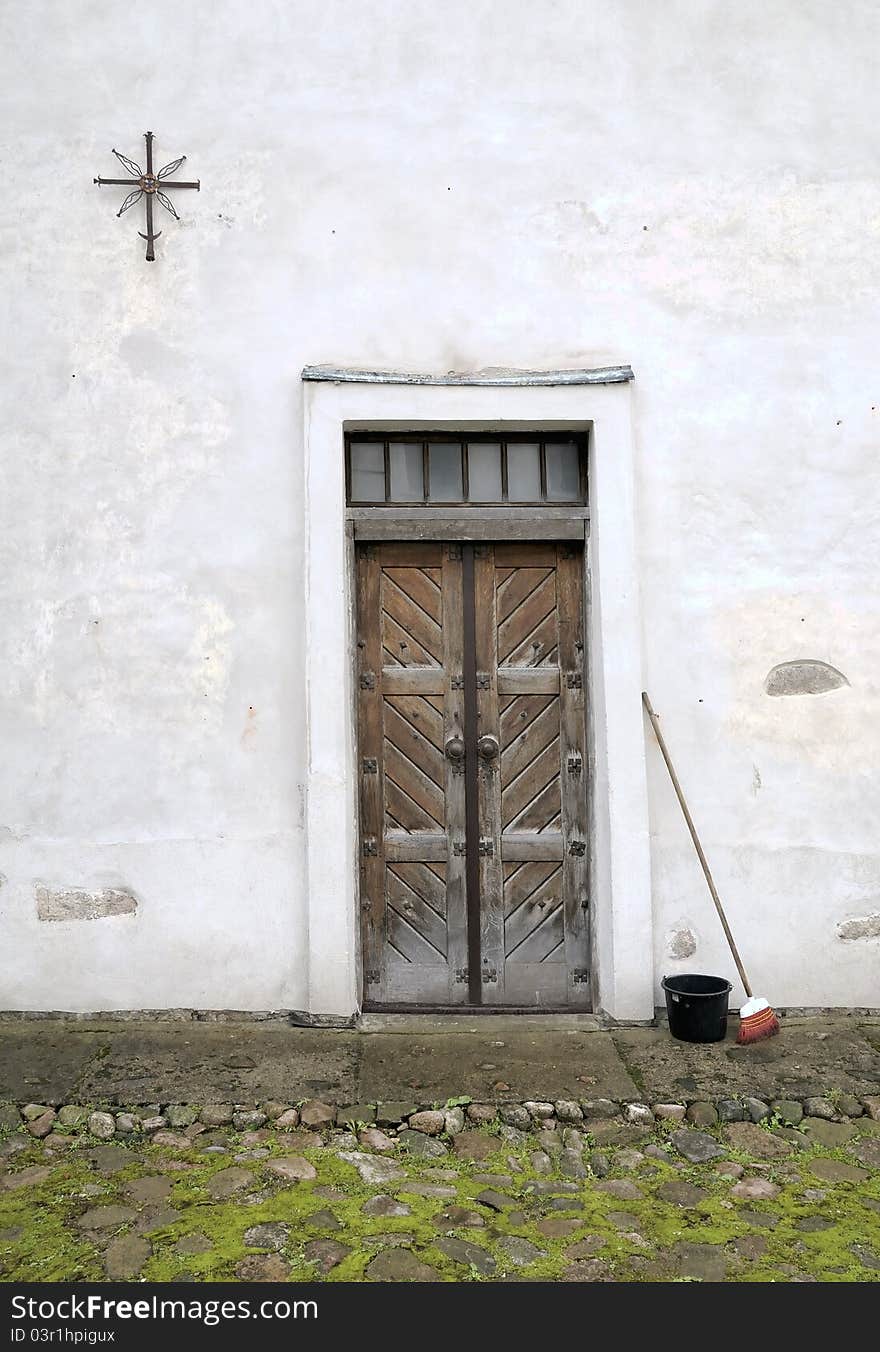 Street. An entrance in monastery. Cross and sun, metal sign. A broom and a bucket for garbage